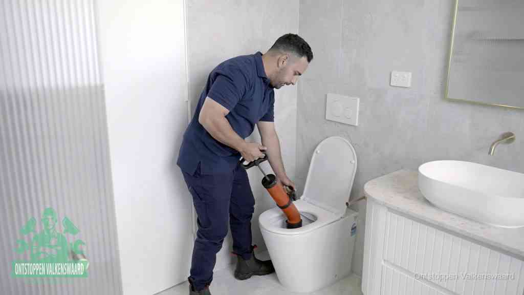 Een monteur buigt over een wandcloset en duwt met de hand een persluchtontstopper in de toiletpot om de verstopping handmatig los te maken in Valkenswaard