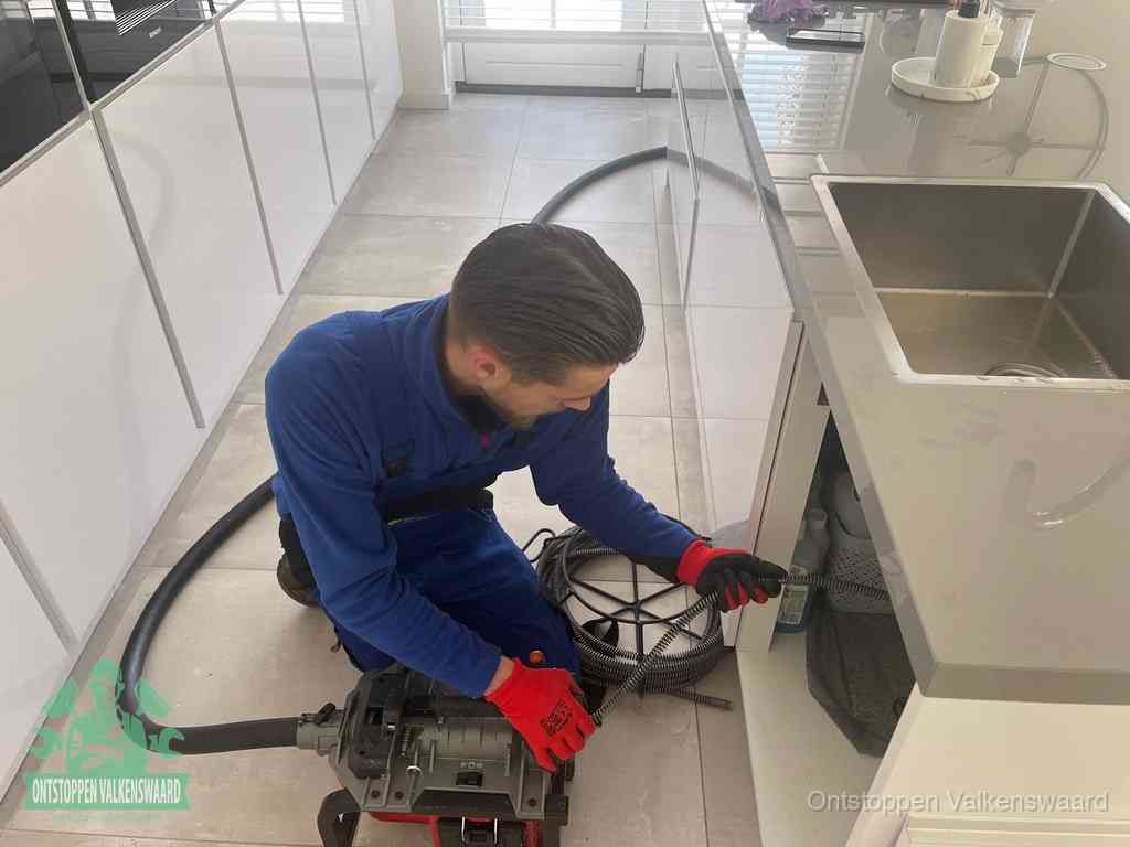 Een monteur ontstopt de keukenafvoer onder de spoelbak met een elektrische veermachine in Valkenswaard