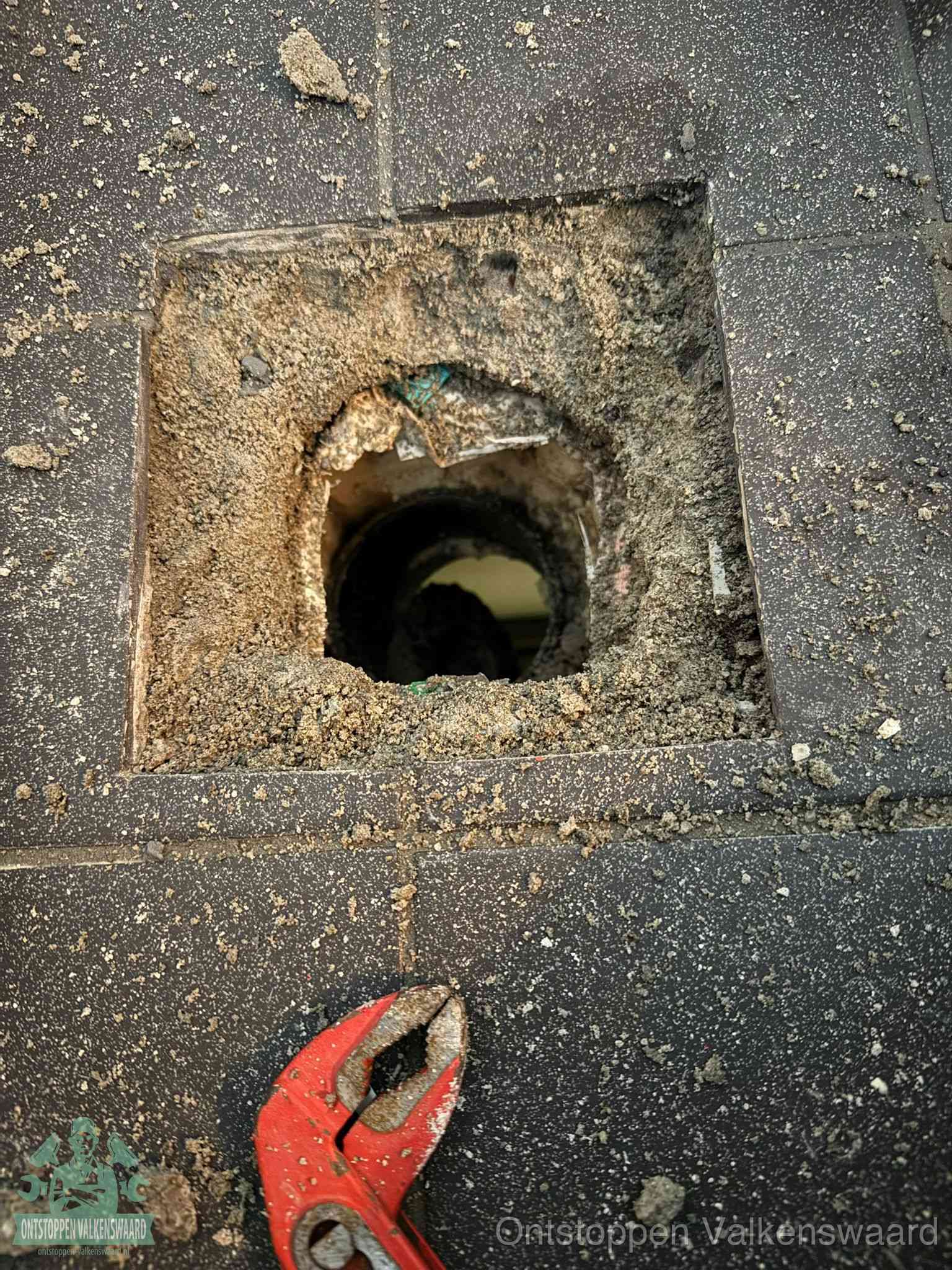 Een geopend rioolputje in een betontegelvloer met losgemaakt rooster en een zichtbare ronde afvoerbuis, het achterhalen waar de afvoerverstopping zit in Valkenswaard