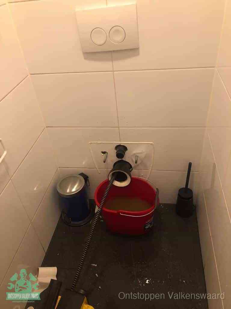 Een ontstopte wand-wc met verwijderde toiletpot waar een ontstoppingsveer in de wanduitgang verdwijnt, het achterhalen waar de verstopping zit in Valkenswaard