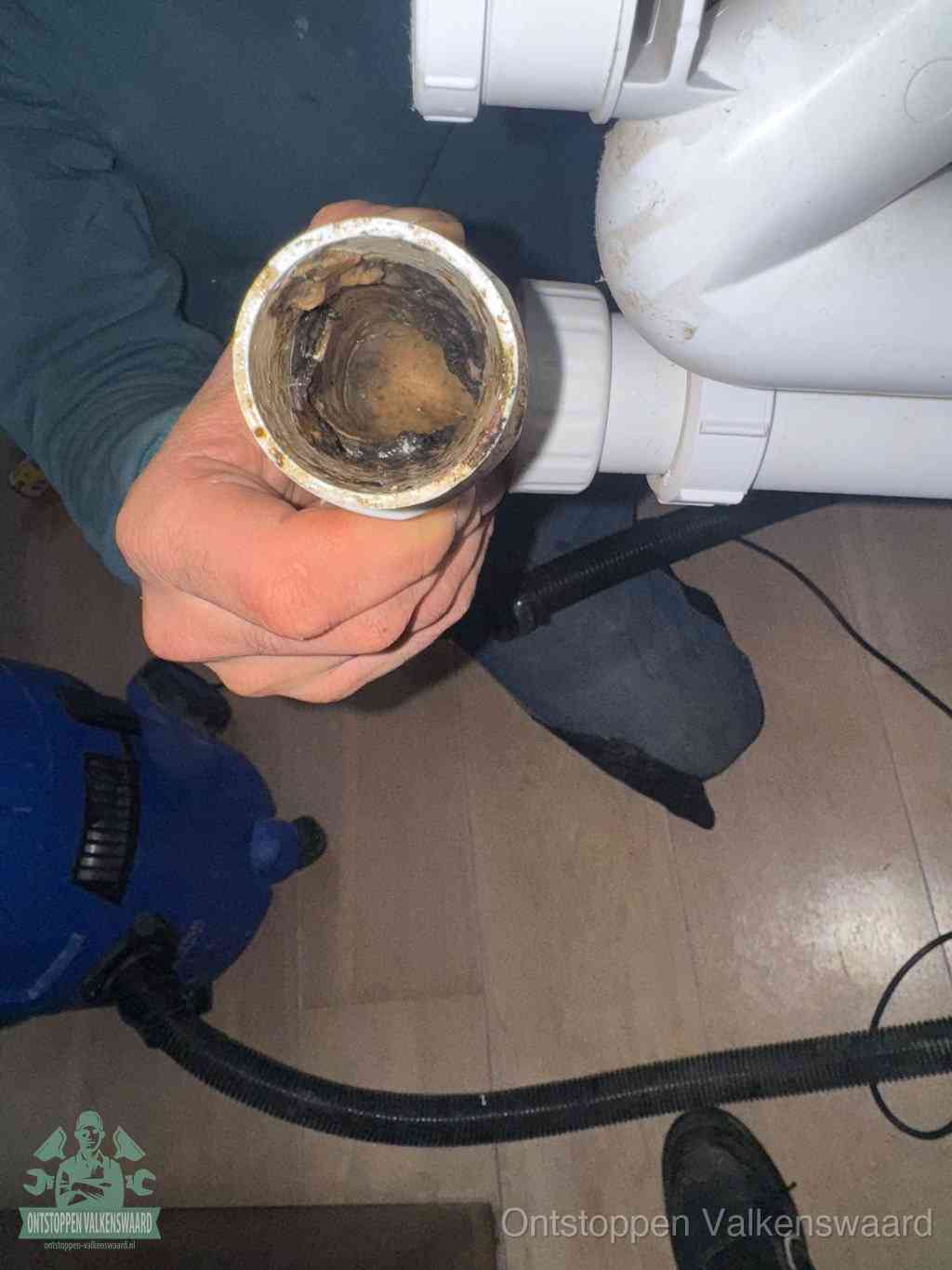 Een hand houdt een losgekoppeld PVC-afvoerbuisstuk vast dat van binnen volledig is dichtgeslibd met vet, vuil en aanslag, de meest voorkomende oorzaak van een verstopte afvoer in Valkenswaard