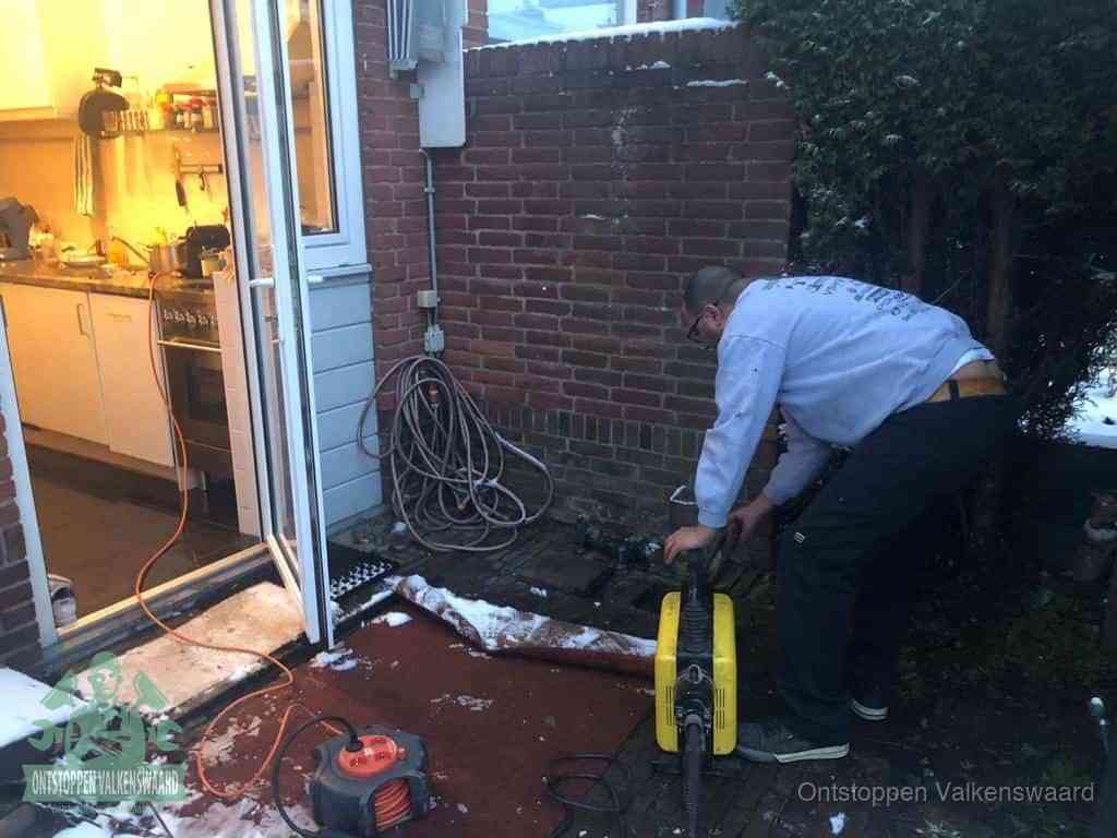 Een monteur werkt buiten bij een open riool-/grondput met een elektrische ontstoppingsmachine om een verborgen afvoerprobleem op te sporen in Valkenswaard