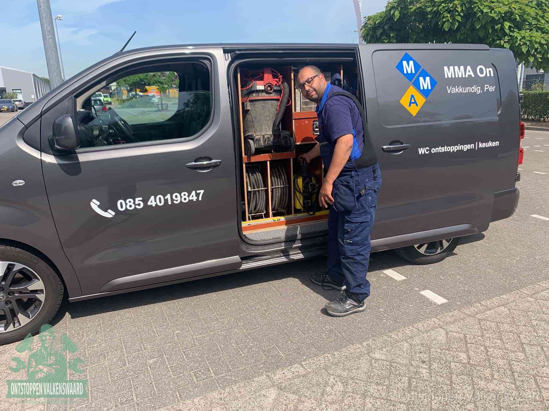Een monteur bij de open schuifdeur van zijn bedrijfsbus op een parkeerplaats, klaar om de oorzaak van terugkerende afvoerverstoppingen aan te pakken in Valkenswaard