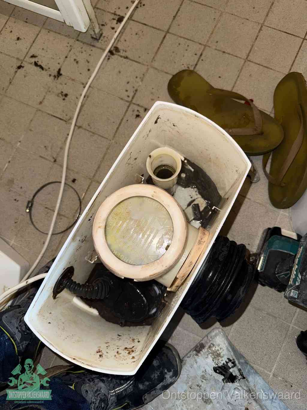 Een gedemonteerde toiletpot op de vloer met ontstoppingsveer en gereedschap ernaast, het verwijderen van een vastzittend voorwerp uit de wc in Valkenswaard