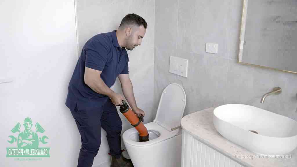 Een man gebruikt een handmatige luchtdruk-ontstopper in een modern betegeld toilet om zelf de wc te ontstoppen in Valkenswaard